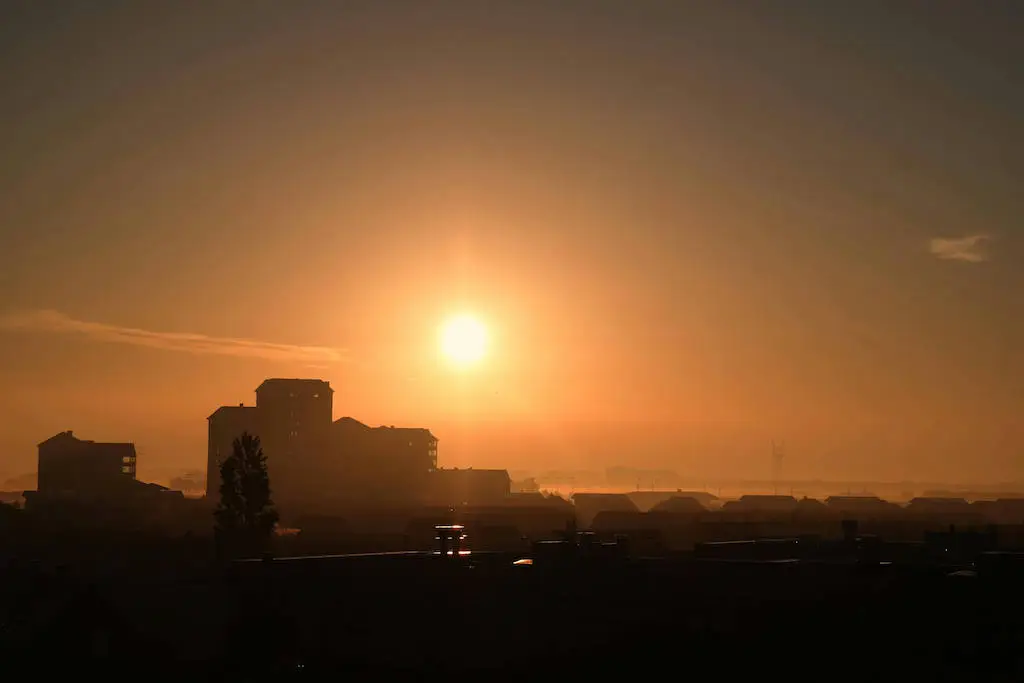Sunrise over a quiet cityscape with silhouetted buildings and a glowing orange sky